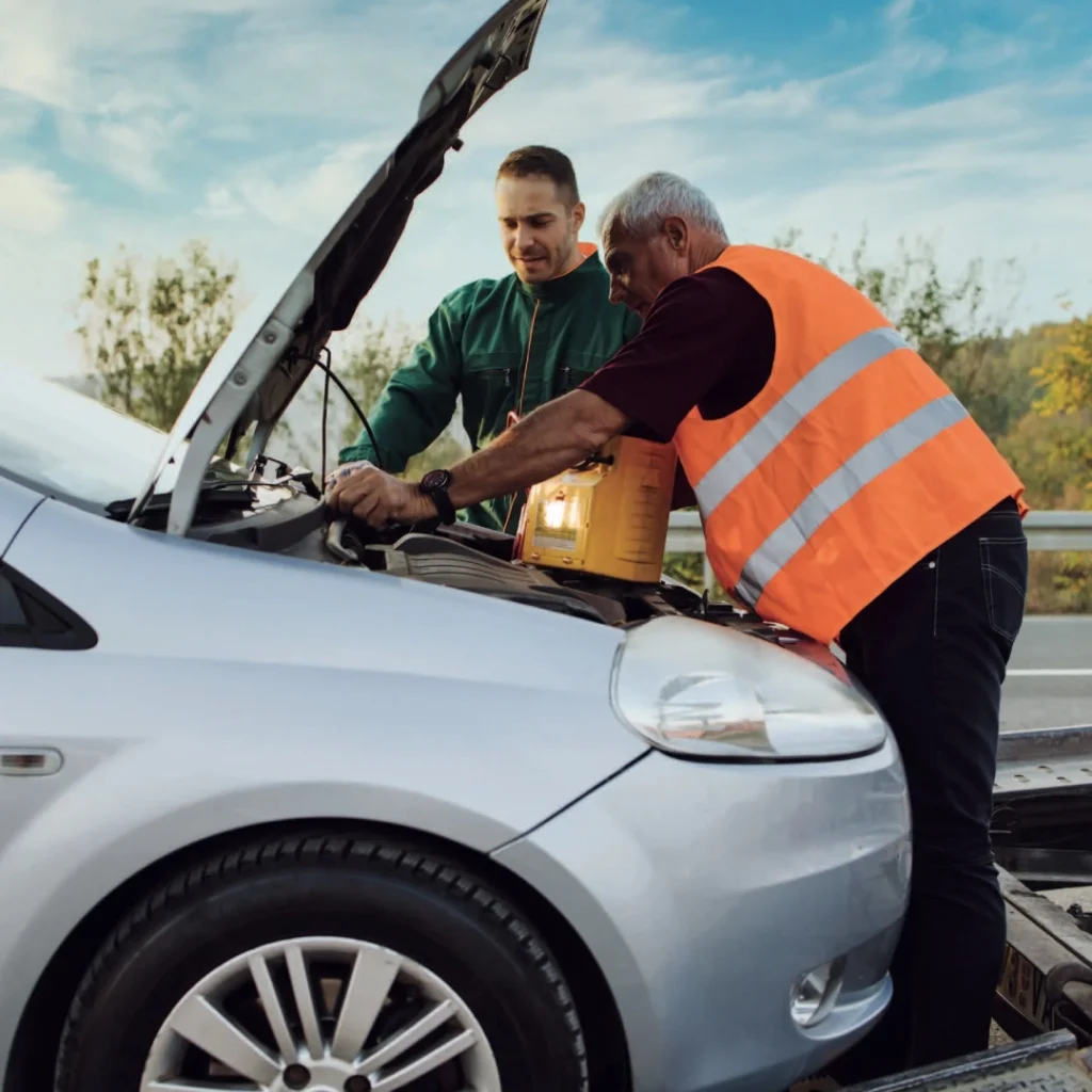 a person in an orange vest standing next to a car with an open hood to jump start it