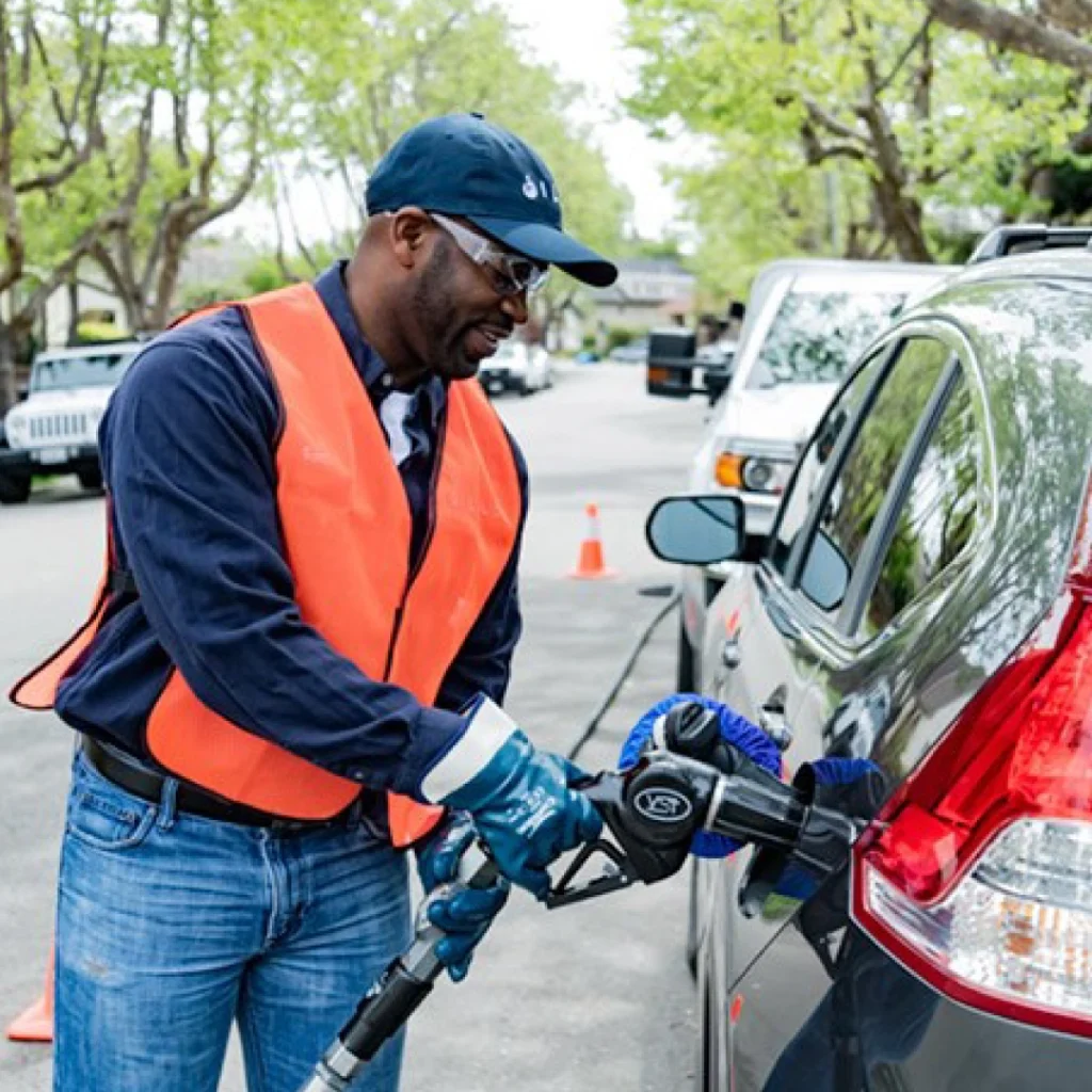 a person in a vest holding a gas pump to a car