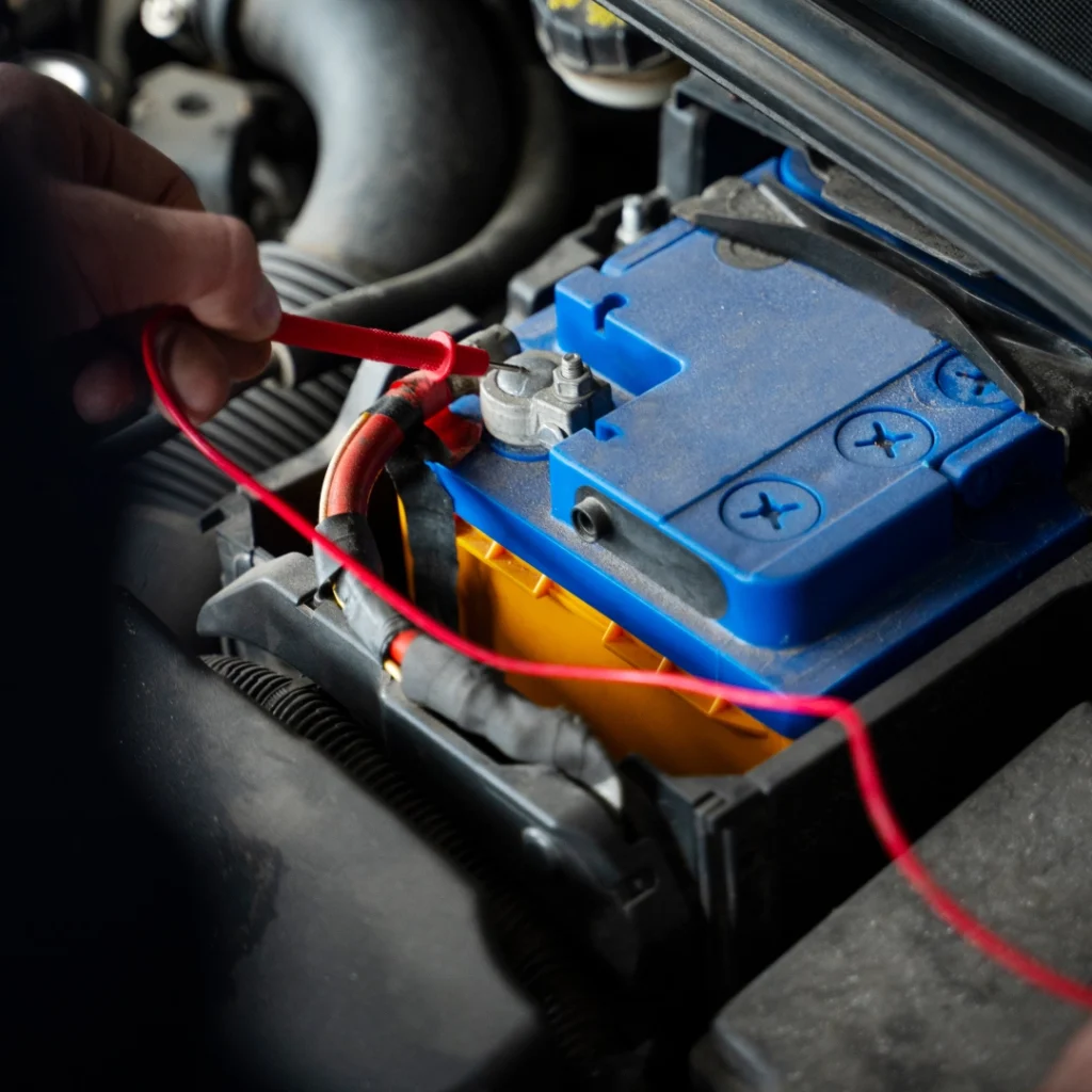 a person holding a red cable in a car engine to jump start it